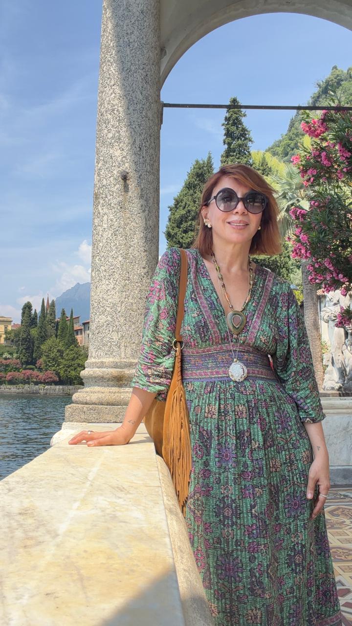 Jasmine in a printed green maxi dress with a fringed suede bag on a lakeside terrace in Italy